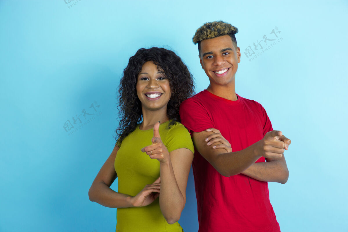 微笑指着 微笑着年轻的情感非洲裔美国人的男人和女人在蓝色的背景上五颜六色的衣服美丽的夫妇黄色女人一起