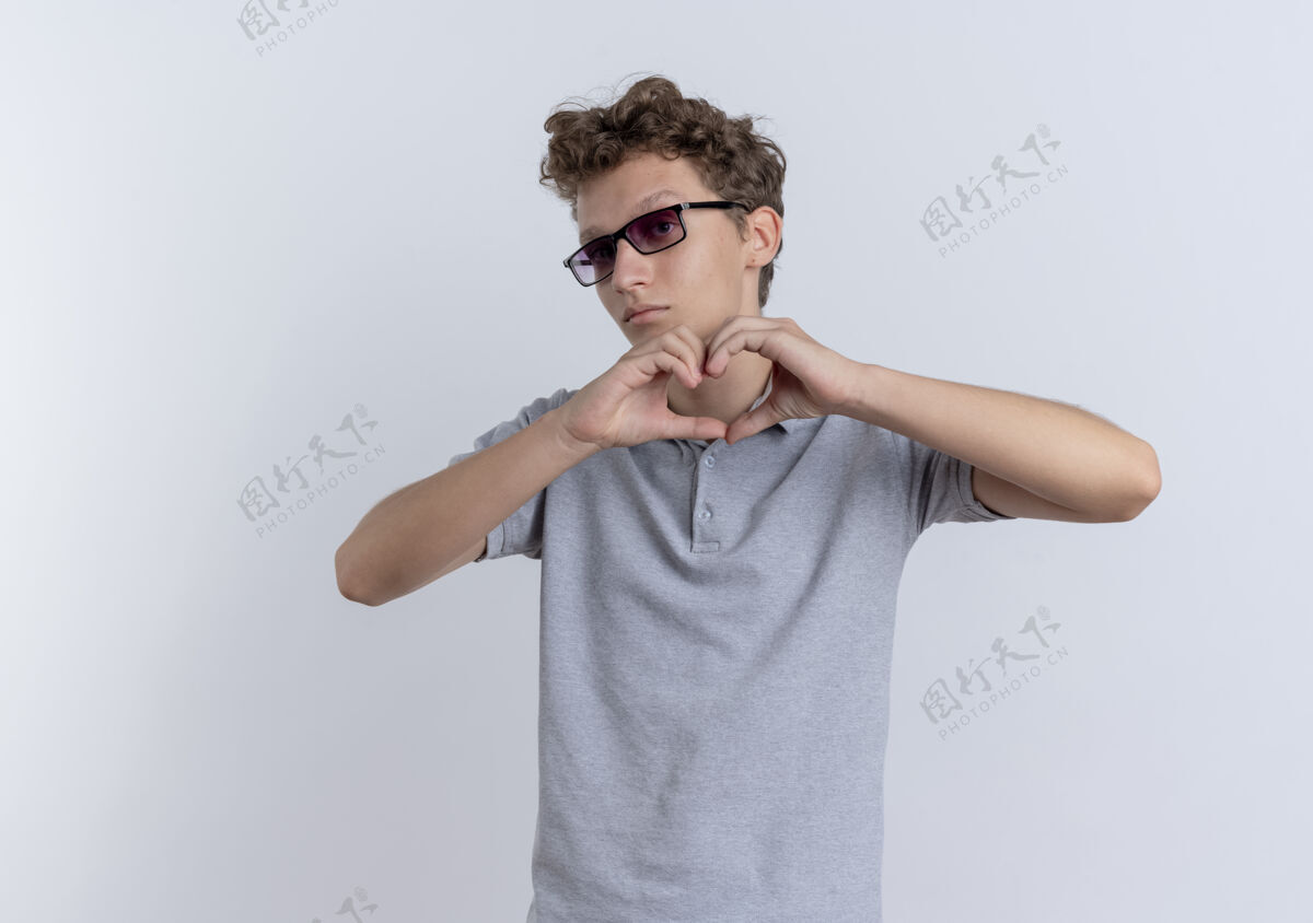 年轻戴着黑眼镜 穿着灰色马球衫的年轻人站在白墙上做着手势手指手势马球