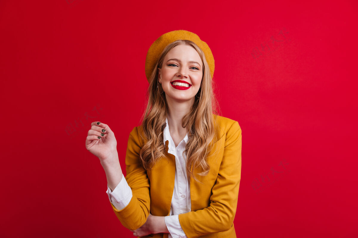 女性幸福的法国女模特在笑红墙上孤立的戴贝雷帽的金发女孩的正面图享受积极手势