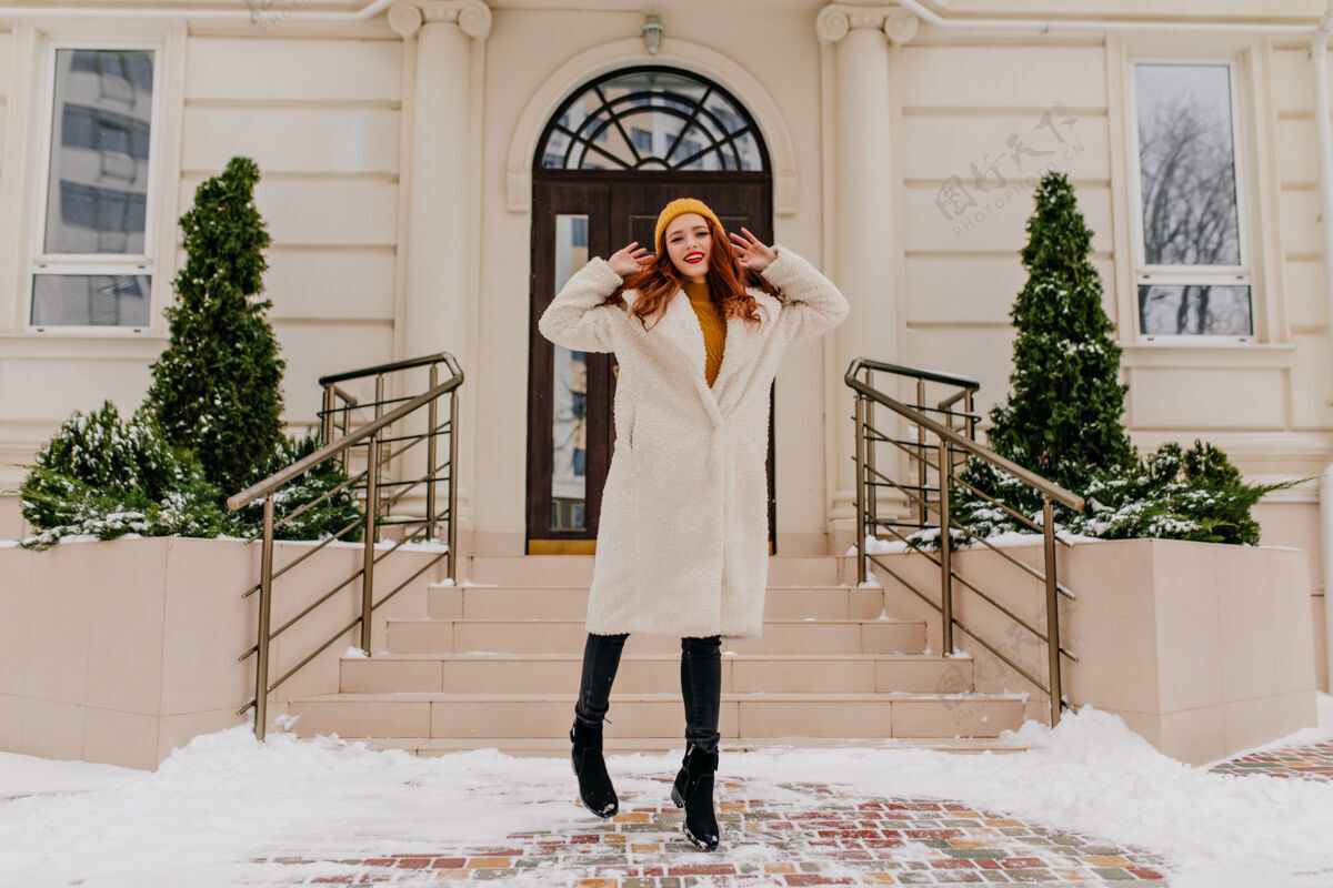 年轻女子穿着冬衣的时尚姜女在漂亮的房子前摆姿势优雅红发女孩的户外镜头户外休闲冬天