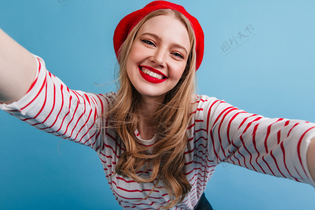 无忧无虑幽默的法国女孩微笑着自拍快乐的金发女模特在蓝色的墙上摆姿势快乐法国年轻人