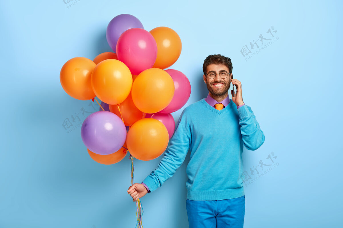 手机穿着蓝色毛衣拿着气球摆姿势的快乐男人男人不刮胡子发型