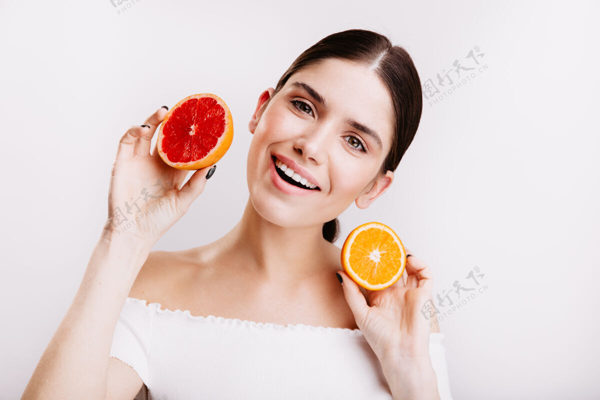 清洁可爱的女孩 在白色的墙上有着友好的微笑没有化妆的女人拿着一片多汁的橘子和葡萄柚模特年轻女人