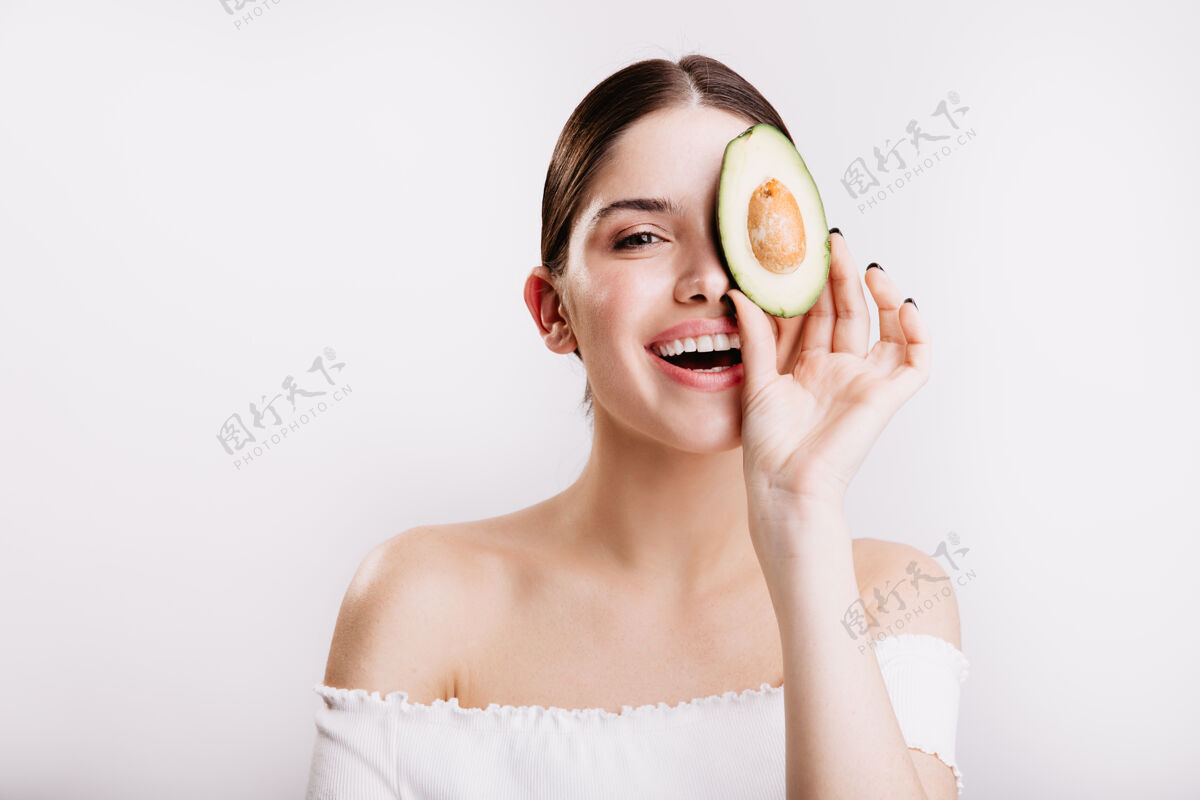 化妆一个没有化妆 皮肤干净的女人微笑着 在白色的墙上摆着一张鳄梨的肖像年轻不化妆女性