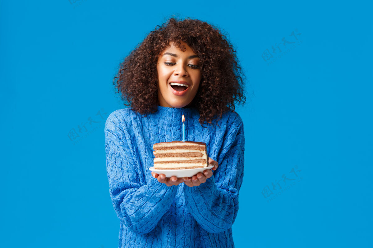 休闲快乐的梦想和充满希望的生日女孩许下愿望迷人的非洲裔美国妇女卷发 吸入空气吹灭点燃的蜡烛美味的b日蛋糕 站在蓝色的墙壁女人微笑欢乐
