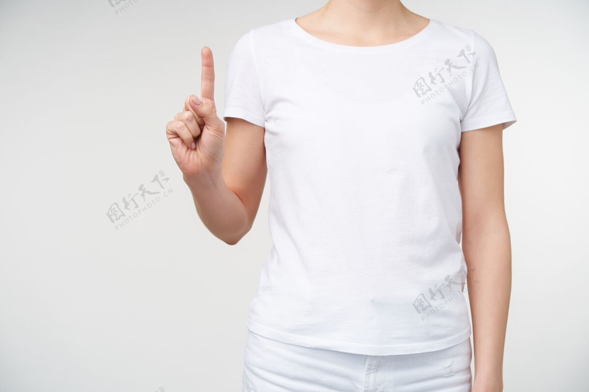 身体摄影棚照片中的年轻女子身穿白色t恤 在白色背景上摆姿势 一边数一边举起食指手和手势的概念手臂计数语言