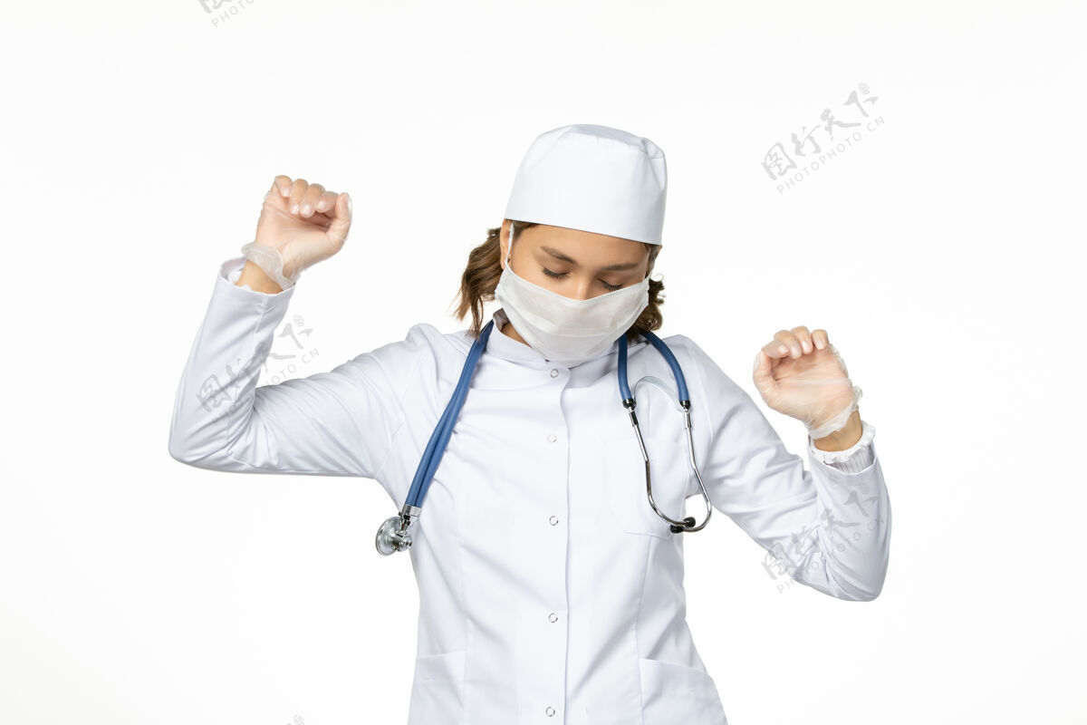轻微正面图年轻女医生带着无菌口罩和手套因冠状病毒在白色表面微微起舞女性听诊器医生
