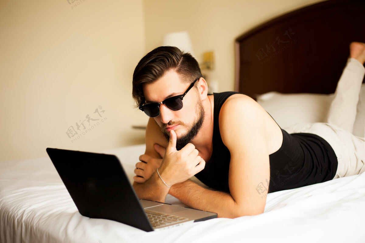 电脑帅气时尚的男人在酒店的户外摆姿势躺在床上经理商务男士放松