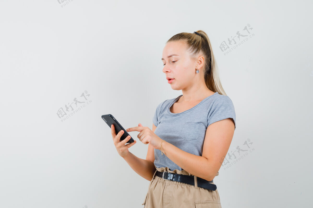 人年轻的女士穿着t恤和裤子用手机 看起来很忙成人欢呼时尚