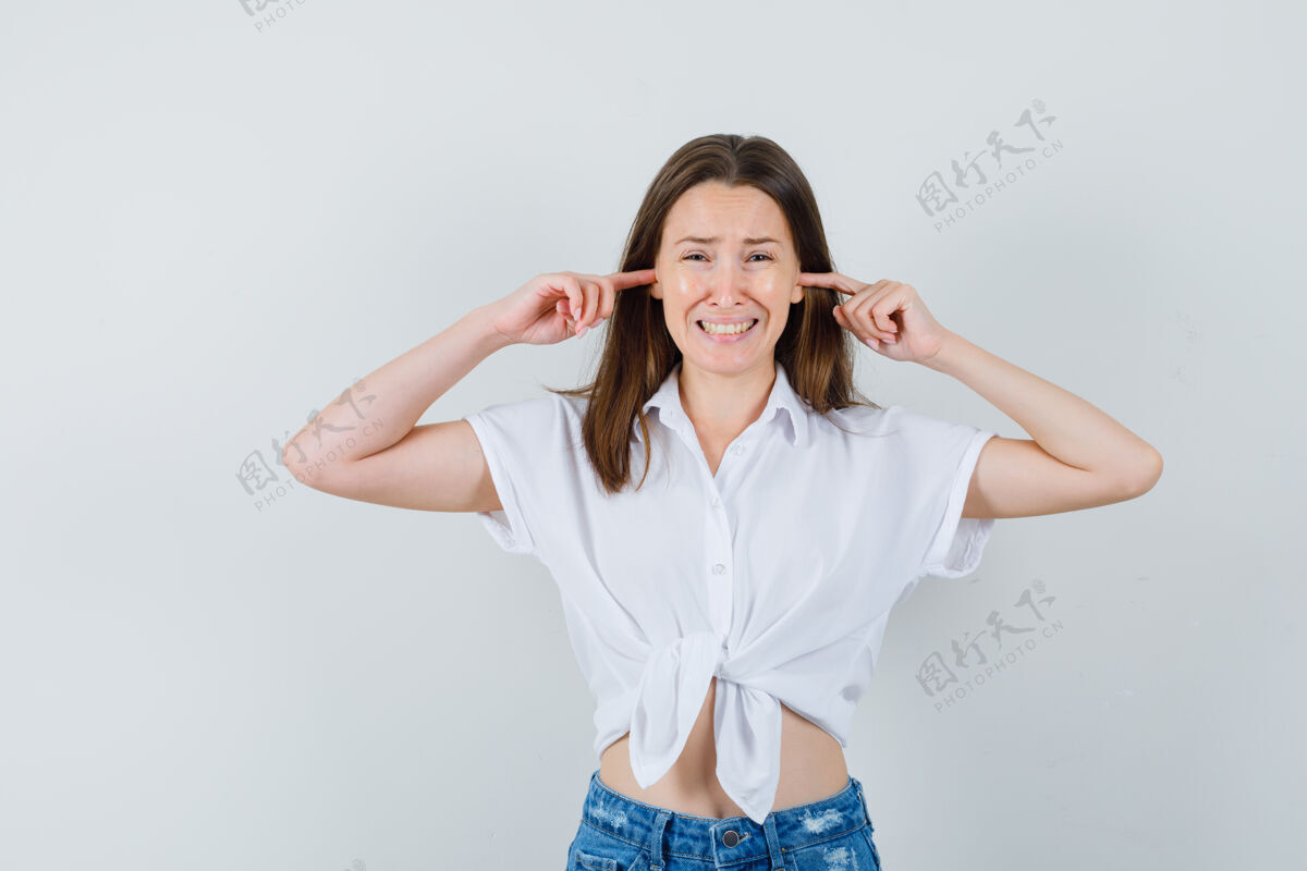 成人穿着白衬衫的年轻女士用手指堵住耳朵 看上去很无聊 正前方视图微笑插头室内