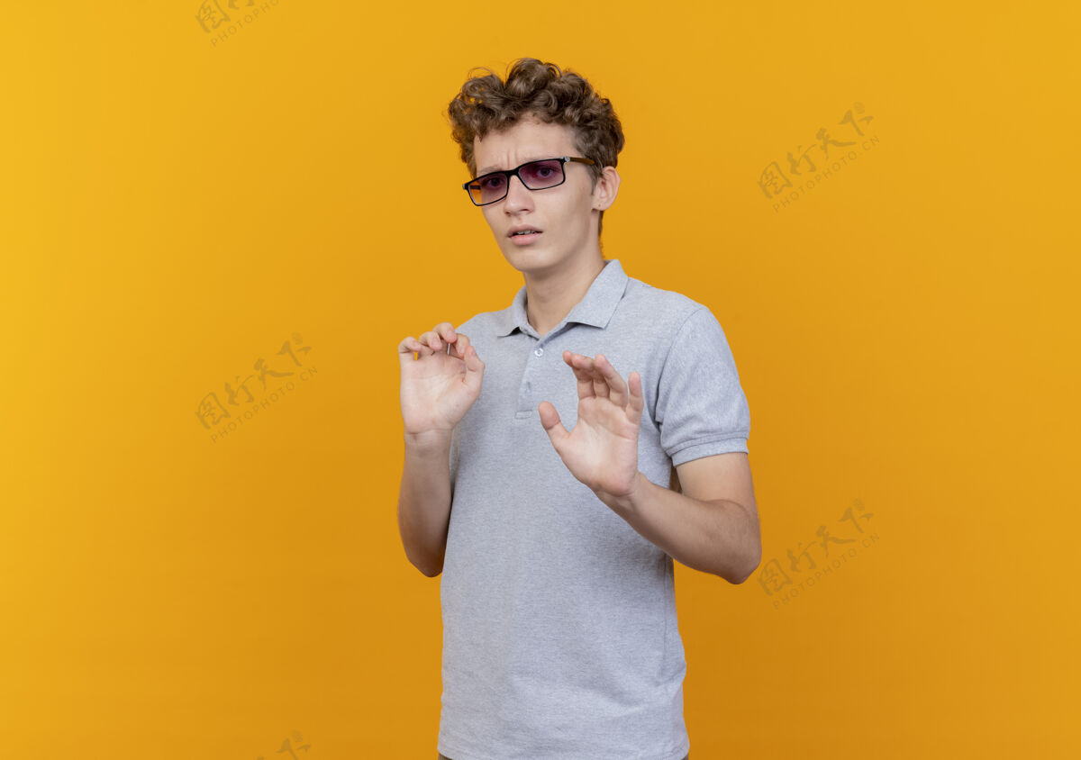 告诉一个戴着黑眼镜 穿着灰色马球衫的年轻人站在橘色的墙上做停车标志 伸出手来告诉大家不要靠近手马球男人
