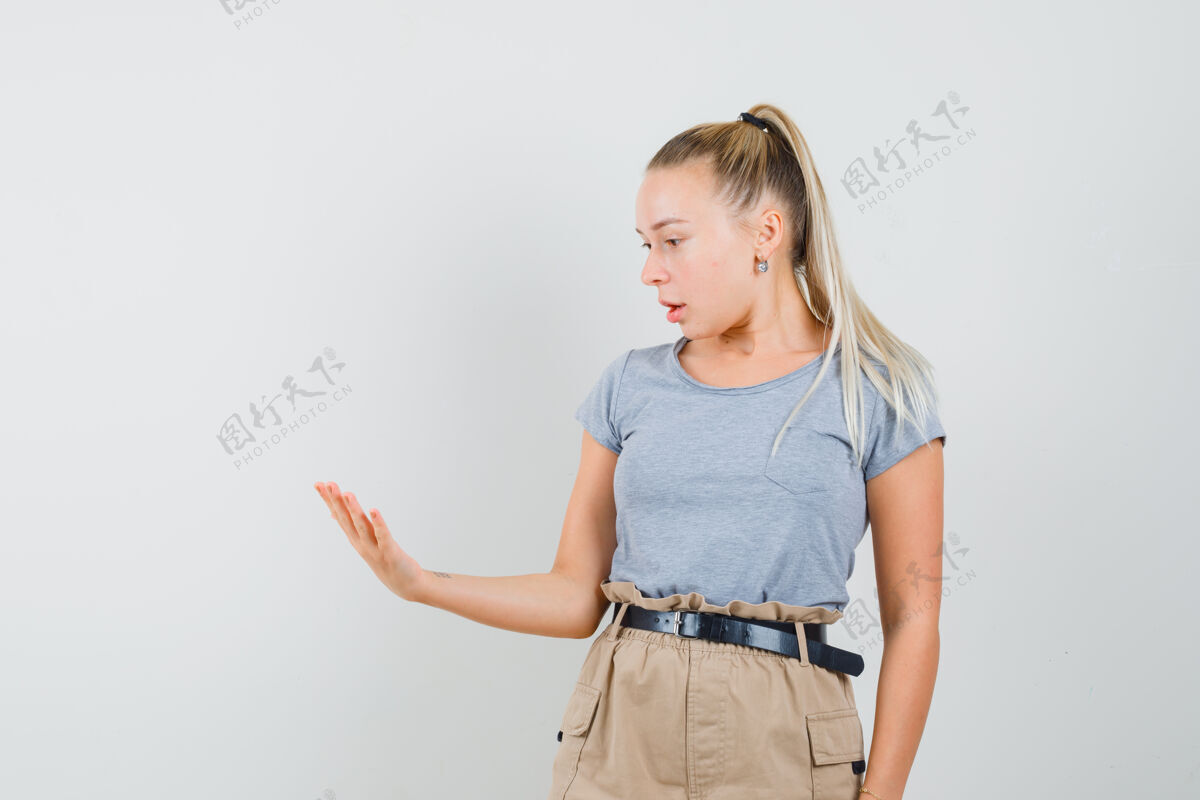时尚穿着t恤和裤子的年轻女士看着她空荡荡的手掌 看起来很惊讶欢呼女人服饰