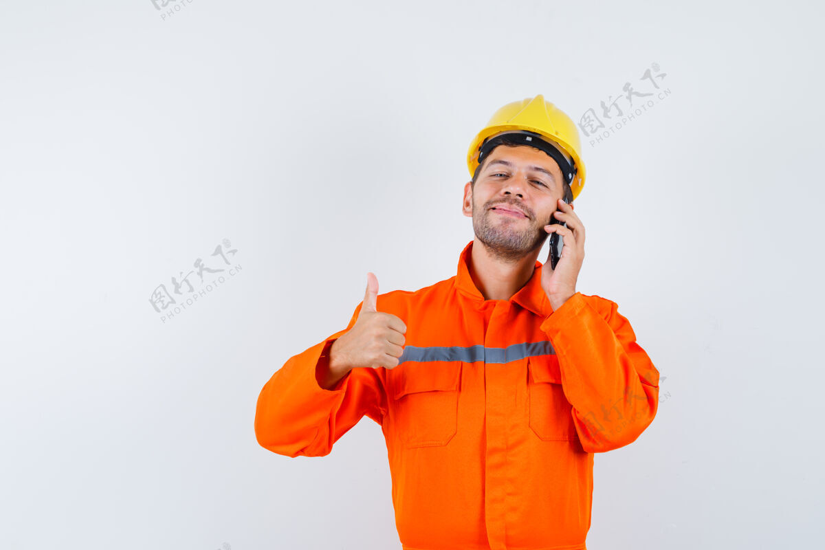 电话穿制服的年轻工人在讲手机 竖起大拇指 看上去很高兴人手机团结