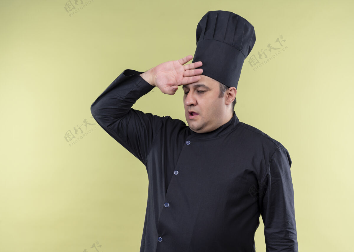 帽子男厨师身穿黑色制服 头戴厨师帽 看上去很累 而且工作过度 手举着头站在绿色背景上男厨师累
