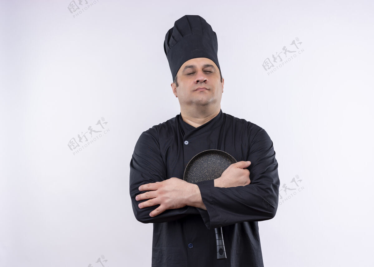 平底锅男厨师身穿黑色制服 头戴厨师帽 举着平底锅 闭着眼睛站在白色背景上制服帽子持有