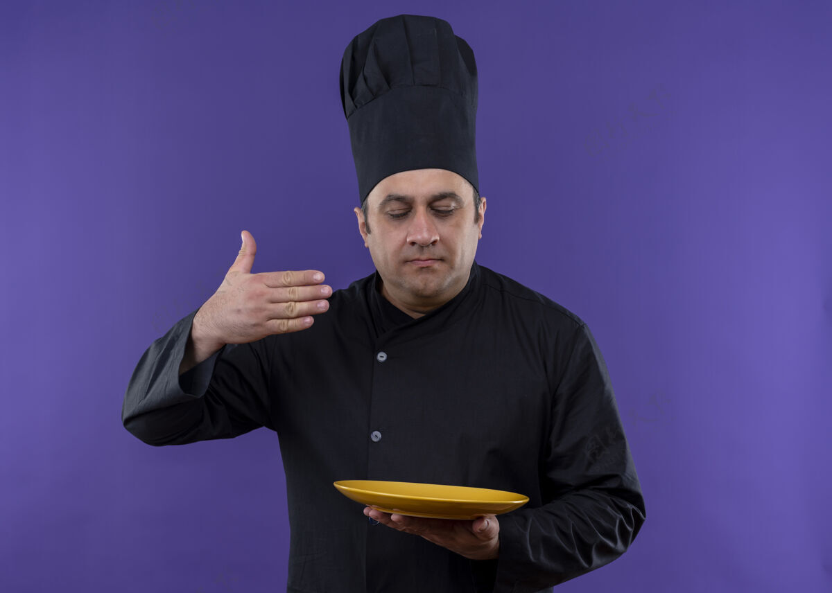 紫男厨师身穿黑色制服 头戴厨师帽 手拿煎锅 站在紫色的背景下 感受着美味的食物闻着制服站着