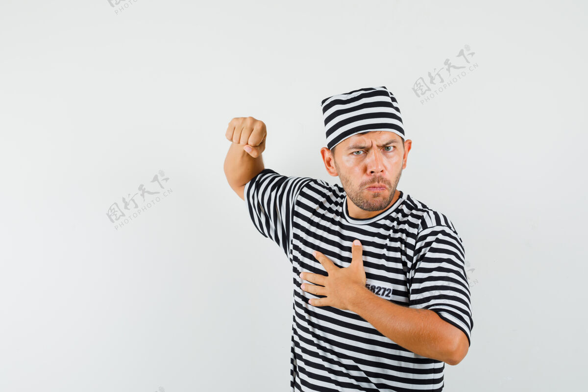 肖像一个穿着条纹t恤 戴着帽子 满脸怒容的年轻人用拳头威胁我胡茬成人胡须