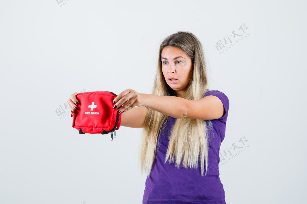 女人年轻女士展示急救箱在紫罗兰色t恤衫 看起来很惊讶 前视图人室内女人