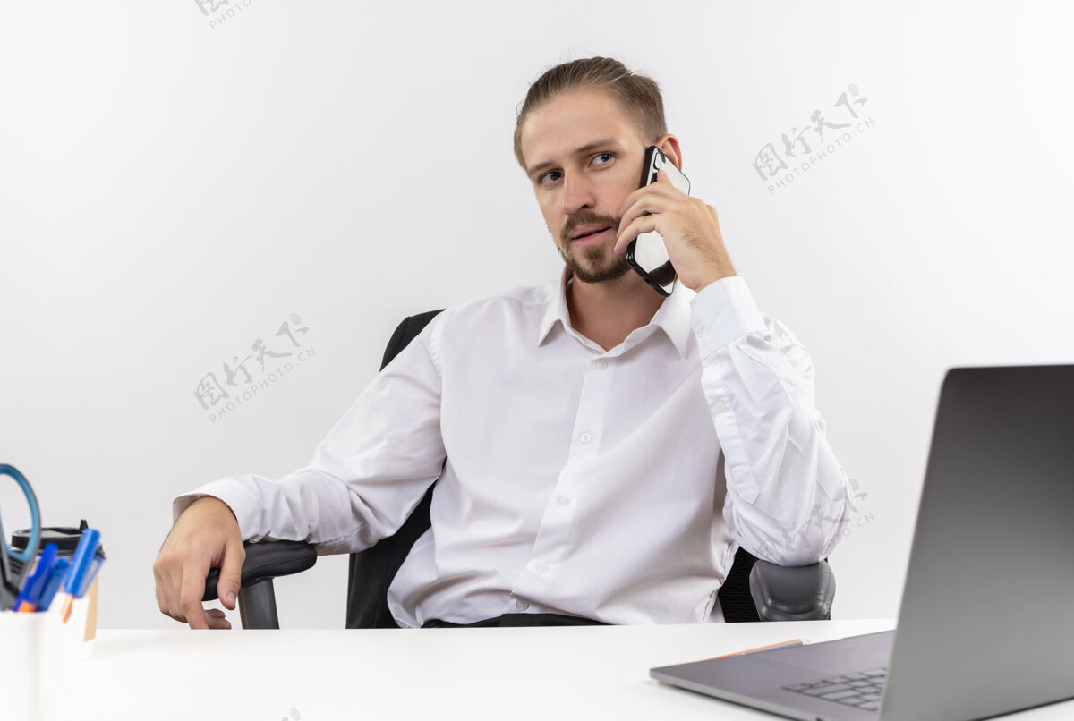 脸穿着白衬衫 戴着耳机 带着麦克风 严肃的脸 坐在白色背景下的办公桌旁用手机聊天的帅哥商人桌子白色靠边站