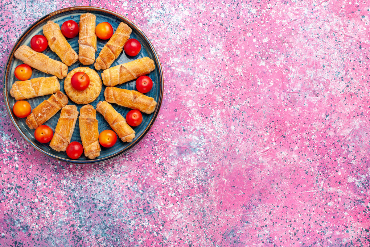 李子顶视图甜美美味的百吉饼烤糕点托盘内与李子在粉红色的办公桌上糖百吉饼水疗