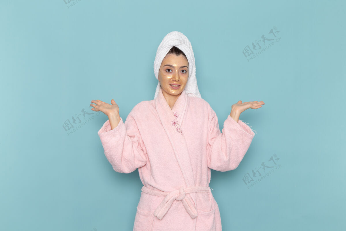 奶油正面图身着粉色浴袍的年轻女性在淋浴后微笑着在蓝色墙壁上享受美丽的水霜自理淋浴浴袍年轻人微笑