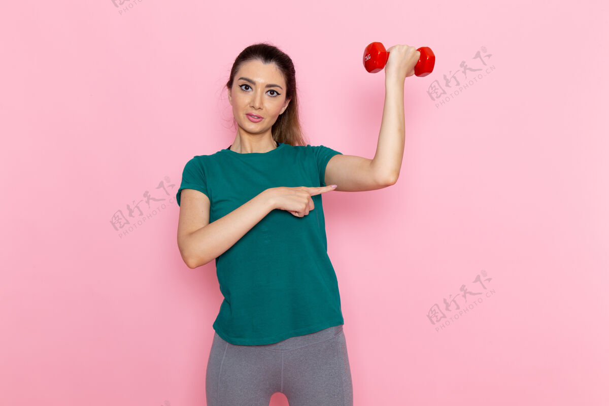 运动正面图年轻女性手持哑铃在浅粉色墙上运动员运动锻炼健康锻炼轻体重人