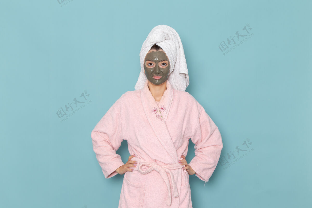 浴袍正面图身着粉色浴袍 脸上戴着面具的年轻女性在蓝色墙壁上摆姿势沐浴清洁美容自护霜封面年轻人淋浴