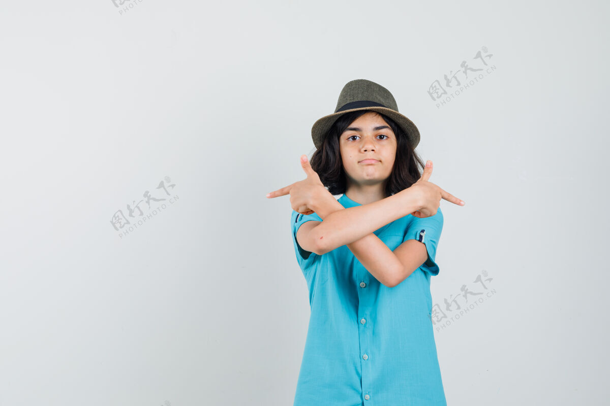 积极穿着蓝色衬衫 戴着帽子的年轻女士交叉着双臂指着不同的侧面 看上去很困惑时尚一起看