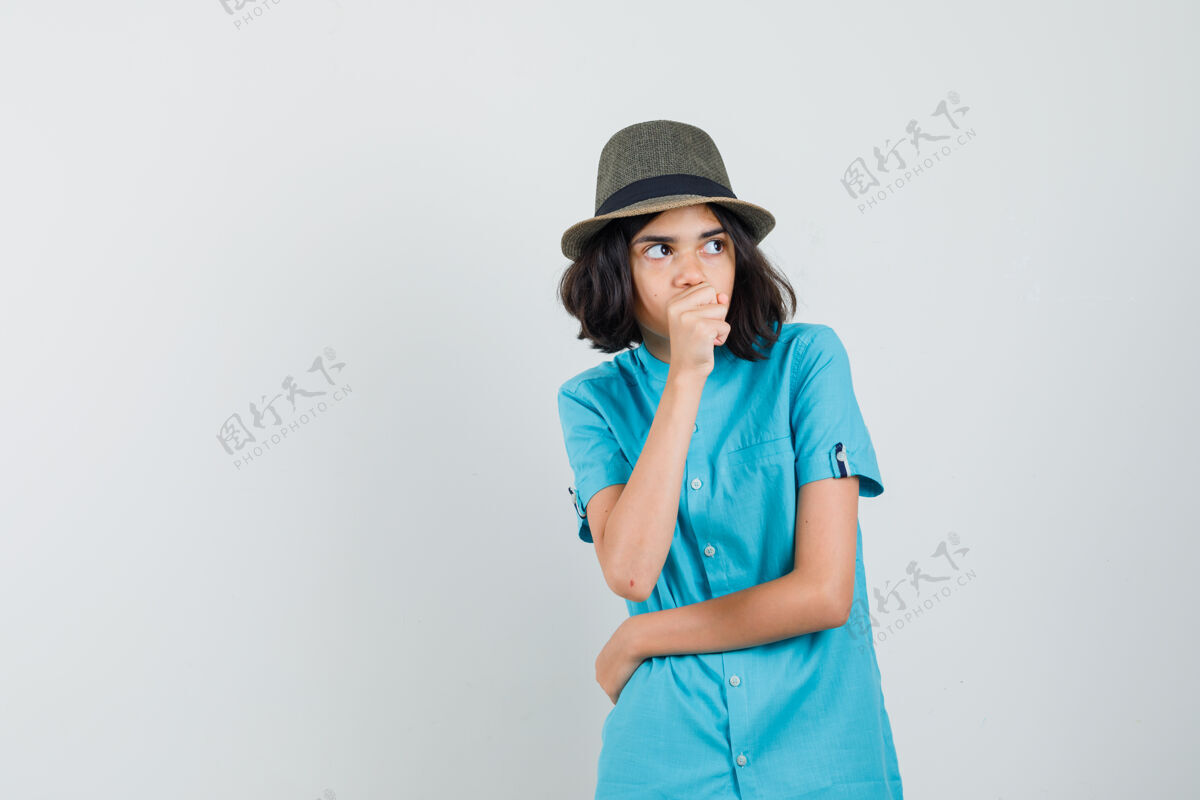年轻年轻的女士用拳头捂着嘴 穿着蓝衬衫 戴着蓝帽子 神情焦急期待喜悦休闲