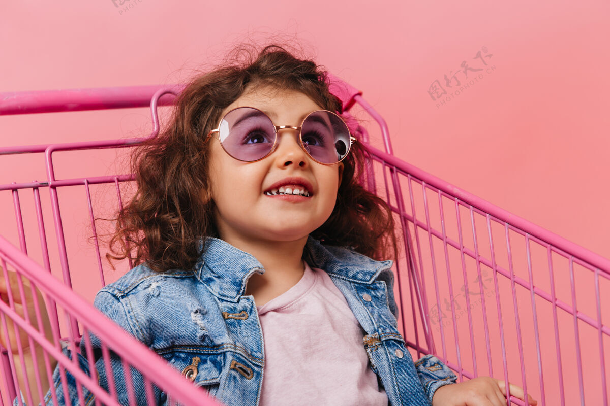 购物车坐在购物车里的学龄前女孩戴着太阳镜的深色小孩笑的摄影棚镜头肖像小孩子