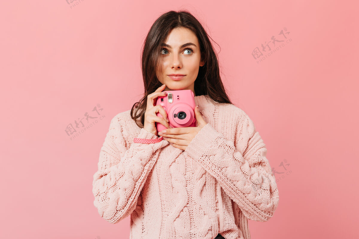 深色迷人的女孩在instax相机上拍照穿着粉色毛衣的女士在孤立的背景上抬起头来微笑蓝色眼睛时尚