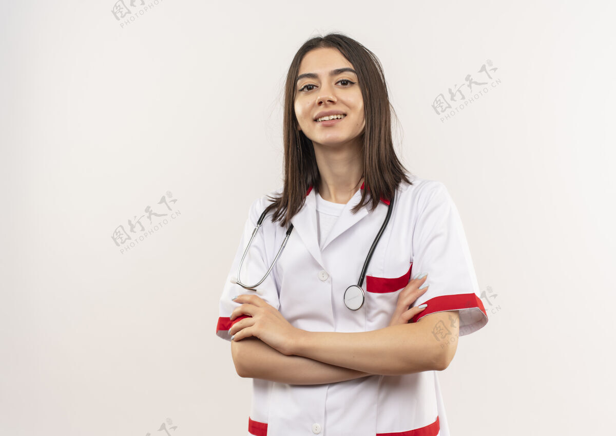 女人年轻的女医生穿着白大褂 脖子上戴着听诊器 手放在胸前 站在白墙上显得很自信手外套人
