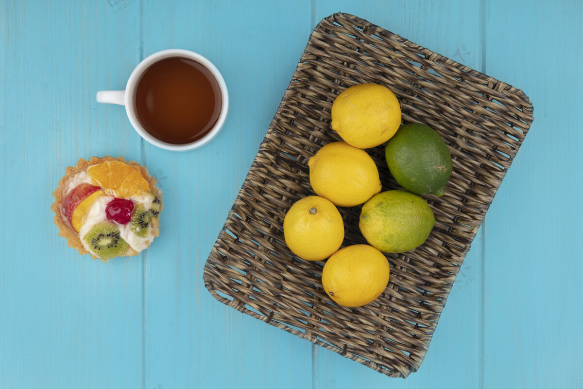 茶一桶新鲜柠檬的顶视图 蓝色木质背景上有一杯茶和水果馅饼木头景观酸