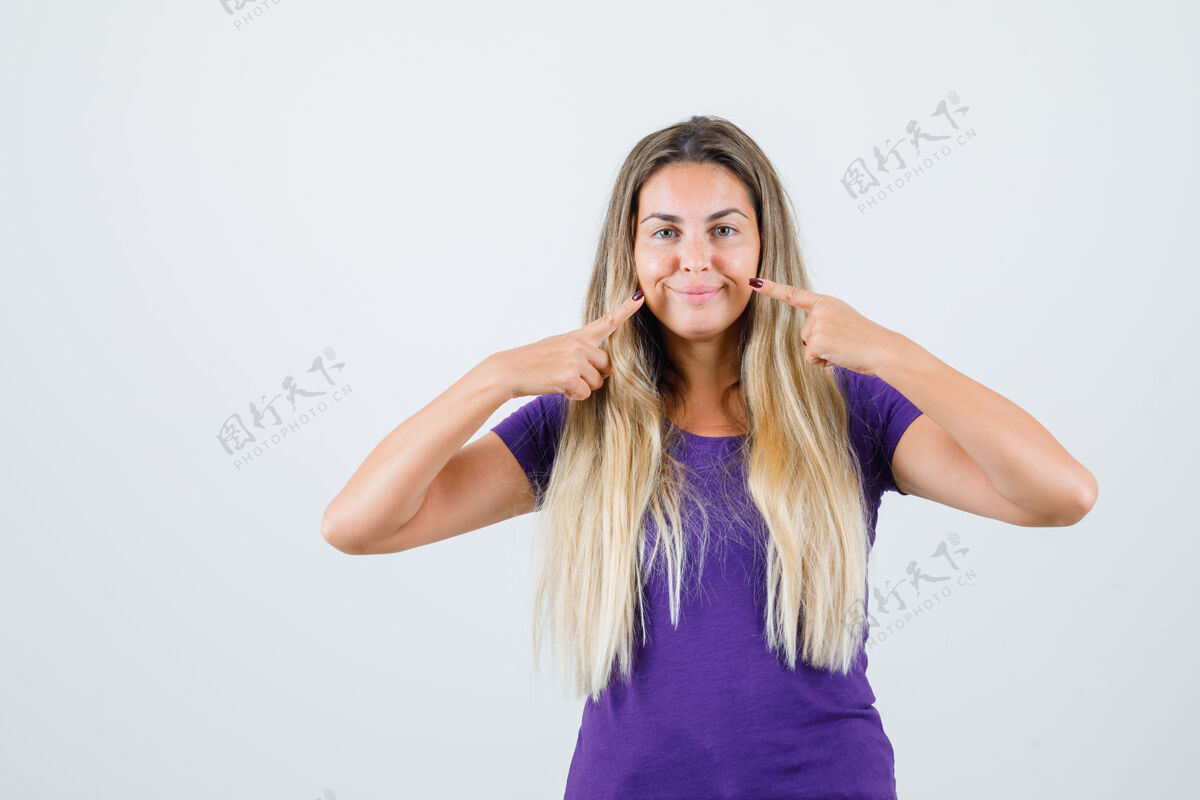 时尚金发女人指着她穿着紫色t恤的微笑 看上去很高兴 正对着前方看金发手可爱