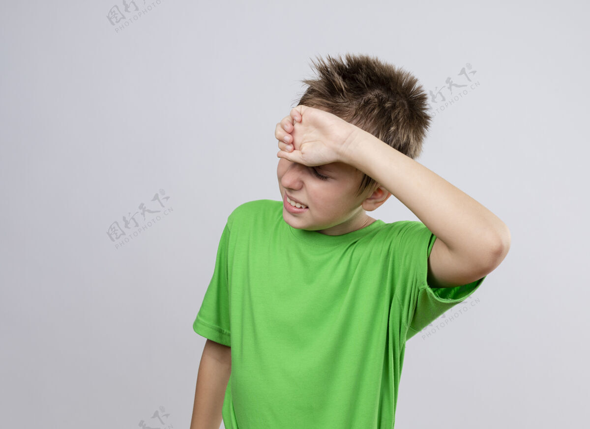 冷生病的小男孩 穿着绿色t恤 站在白墙上摸额头 感觉不舒服站病感觉