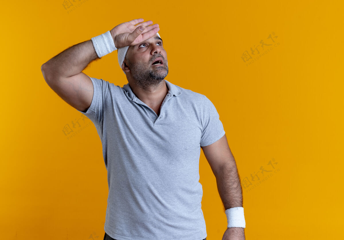 站成熟的运动型男人戴着头巾 站在橙色的墙上 手放在头上 看起来很疲惫手后运动