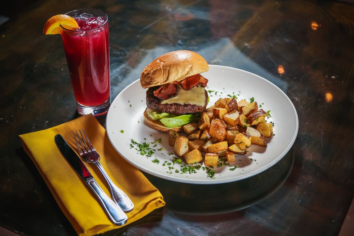 一餐高角度拍摄的一个奶酪汉堡包与土豆方块的一边与一个红色的饮料旁边芝士汉堡肉类牛肉