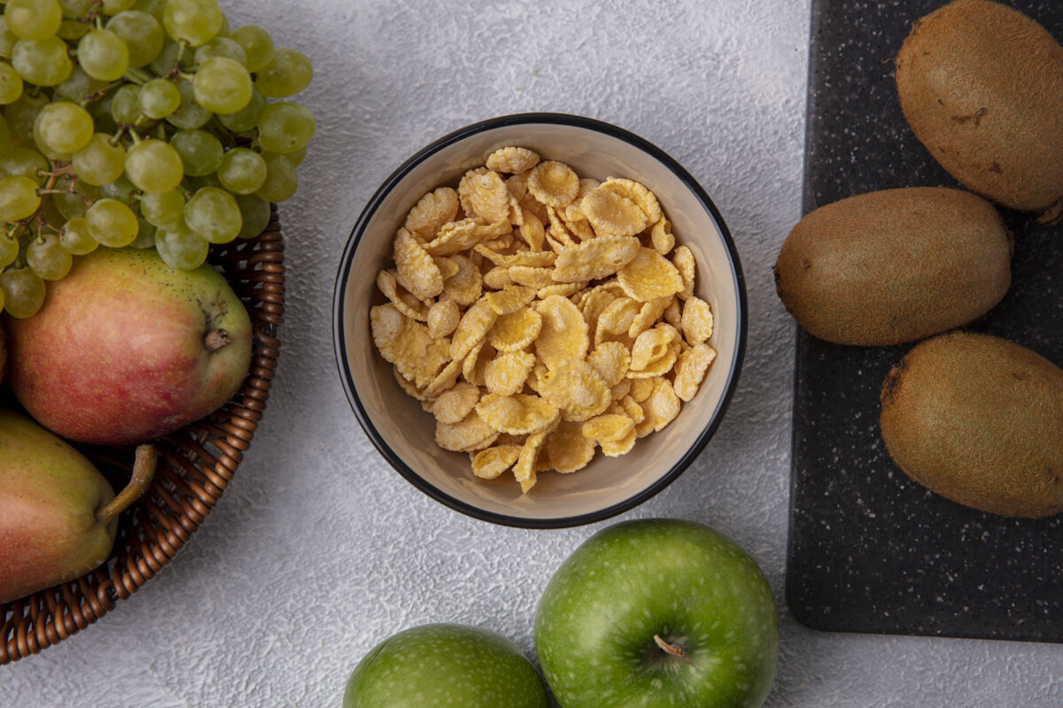 碗顶视图玉米片在一个碗里 绿色的苹果 奇异果和绿色的葡萄在白色的背景上苹果早餐顶部