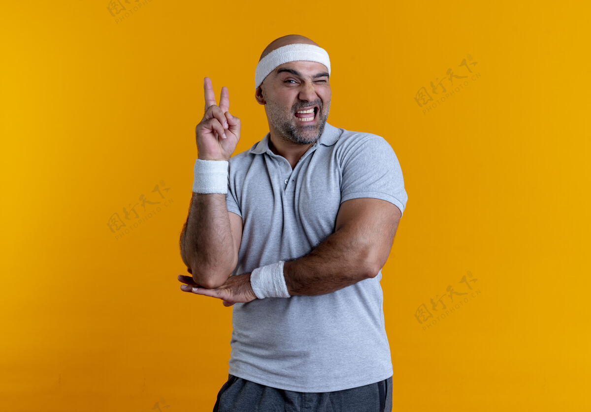 市民戴着头巾的成熟运动型男子望着前方 面带微笑 在橙色的墙上展示胜利标志胜利欢呼人