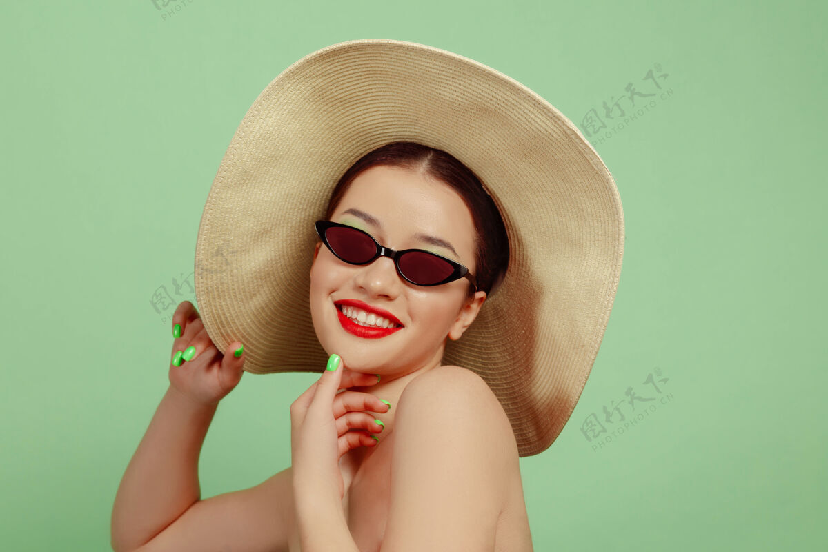 看起来美丽女人的肖像 明亮的妆容 帽子和太阳镜在绿色的工作室背景上时髦和时尚的制作和发型夏天的颜色美丽 时尚和广告概念微笑保持女性新鲜