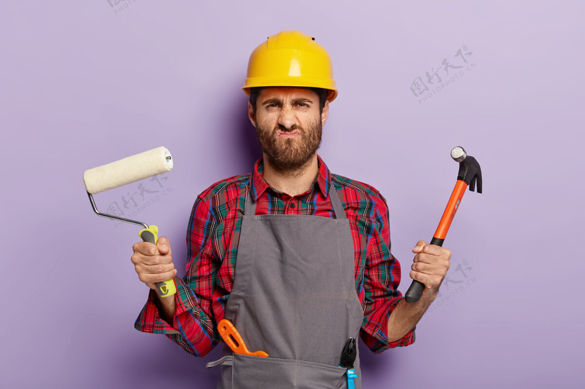 专业不高兴的男建设者的照片微笑着脸与不高兴的表情工人头盔帽子