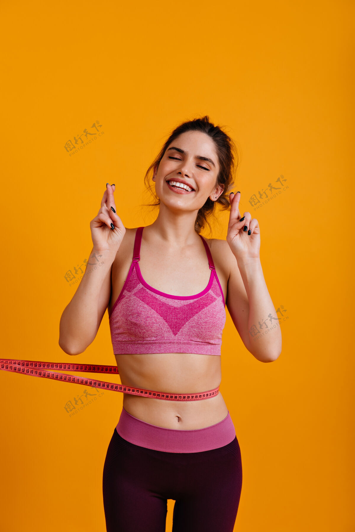 女模特兴奋的女人用卷尺隔离在黄色的墙上运动交叉健身身体