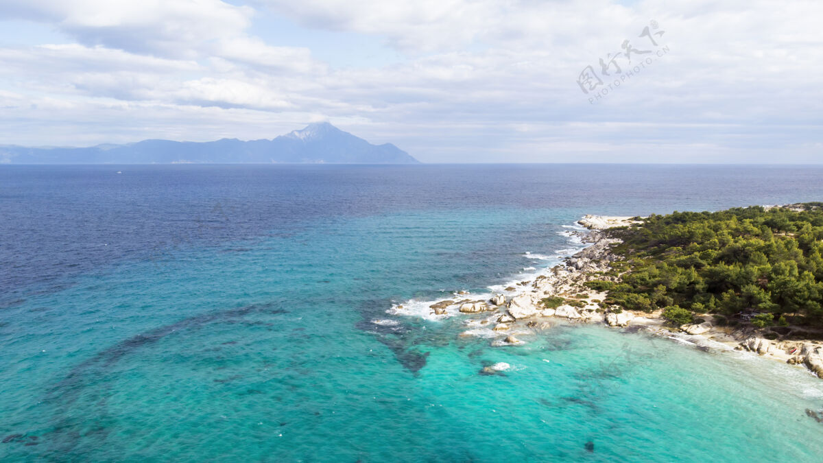 悬崖爱琴海沿岸有蓝色透明的海水 周围绿树成荫 岩石 灌木丛和树木 从无人机希腊俯瞰山爱琴海海湾
