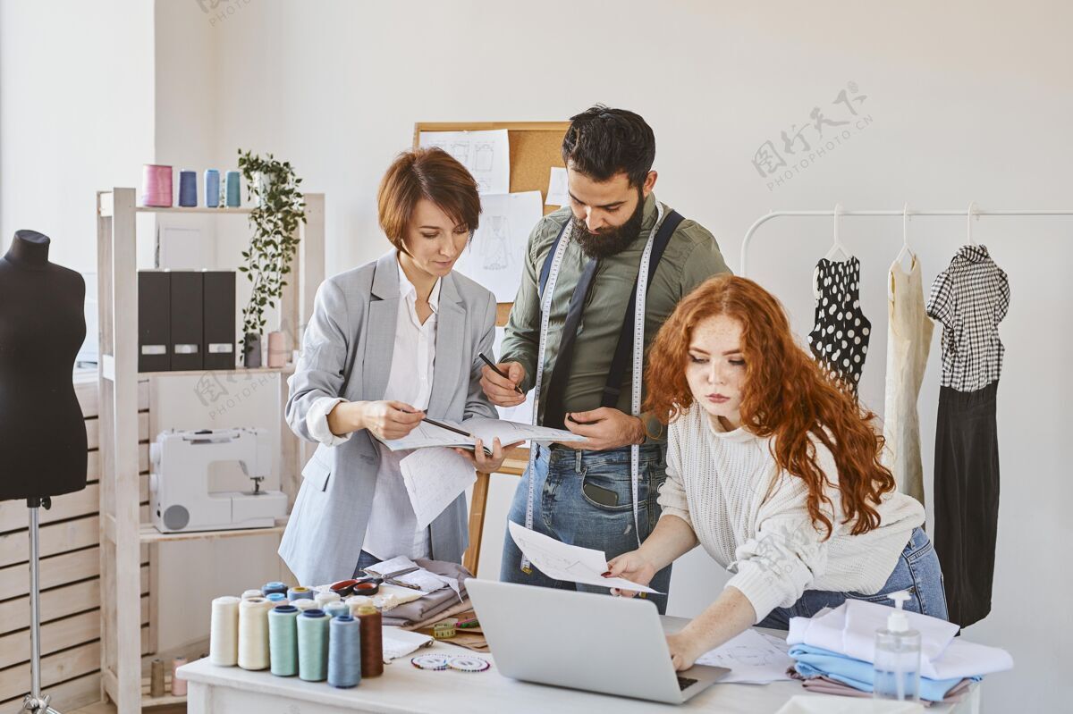 个人由三位时装设计师组成的团队 他们在工作室里用笔记本电脑和纸张工作服装师时装师服装