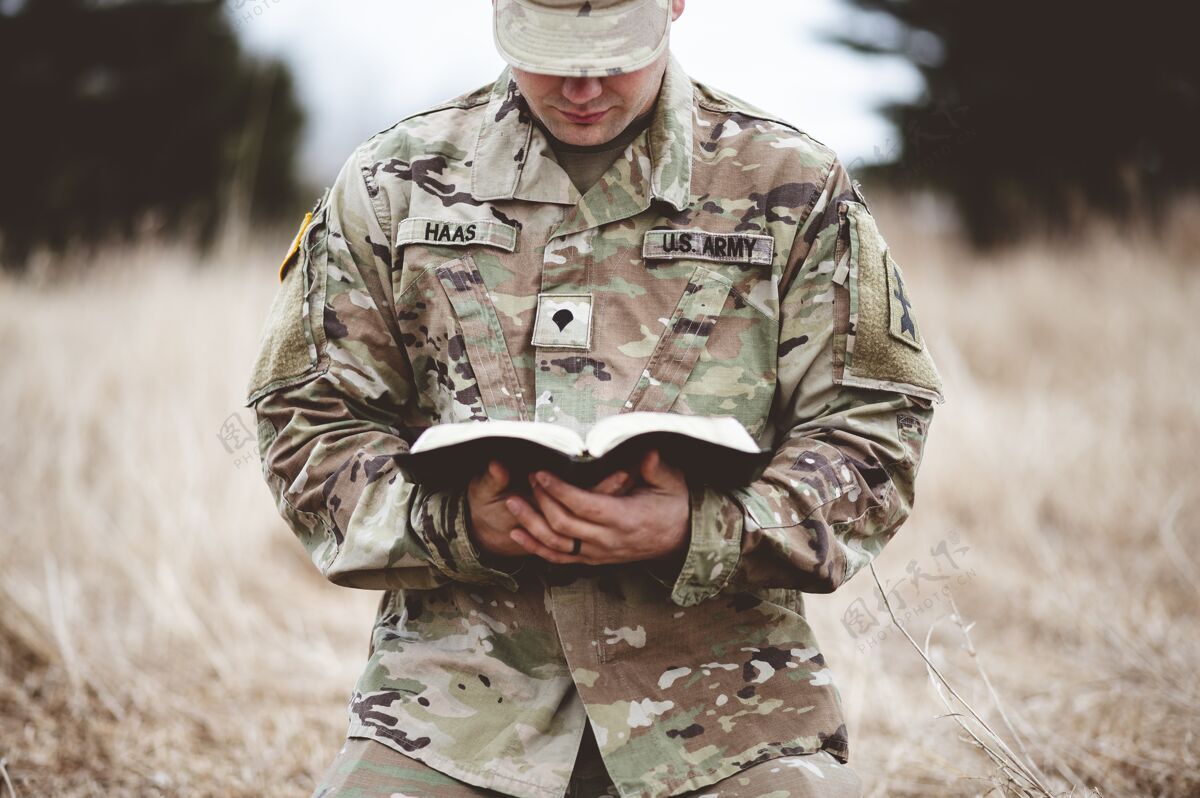 保护浅焦拍摄一个年轻士兵跪在干草上读圣经男性战士保护者