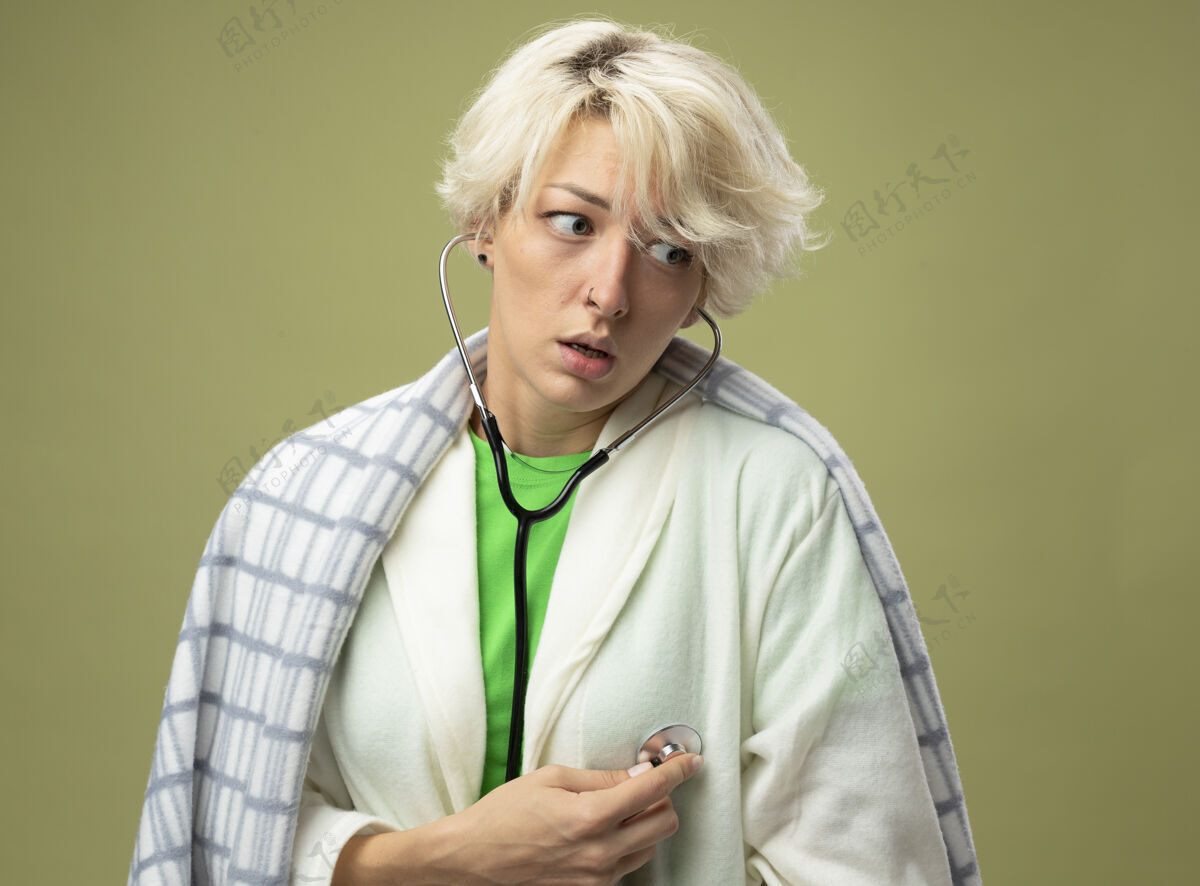 包裹有病的不健康的女人 短发裹在毯子里 用听诊器听她站在光墙上的心跳 感觉不舒服女人毯子不健康