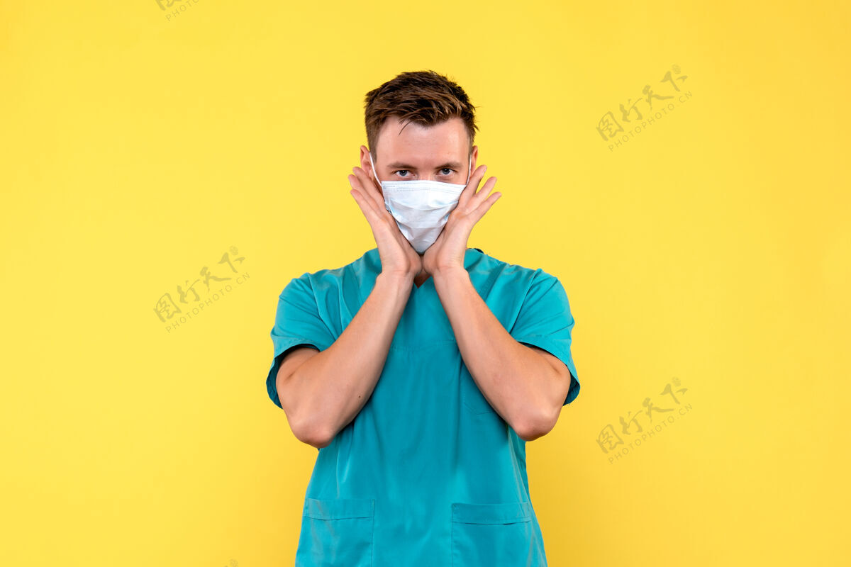 专业黄墙上戴着无菌口罩的男医生的正视图快乐情绪微笑