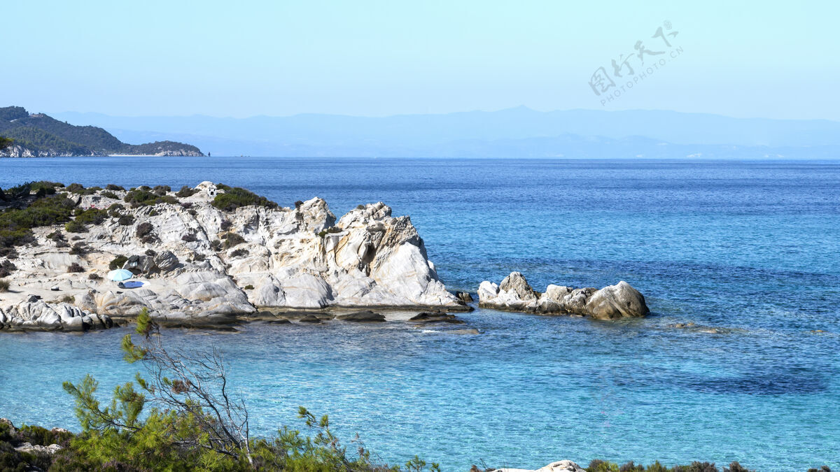 海岸线爱琴海海岸周围绿树成荫 岩石和灌木丛 蓝色的海水和休息的人 希腊悬崖希腊海岸