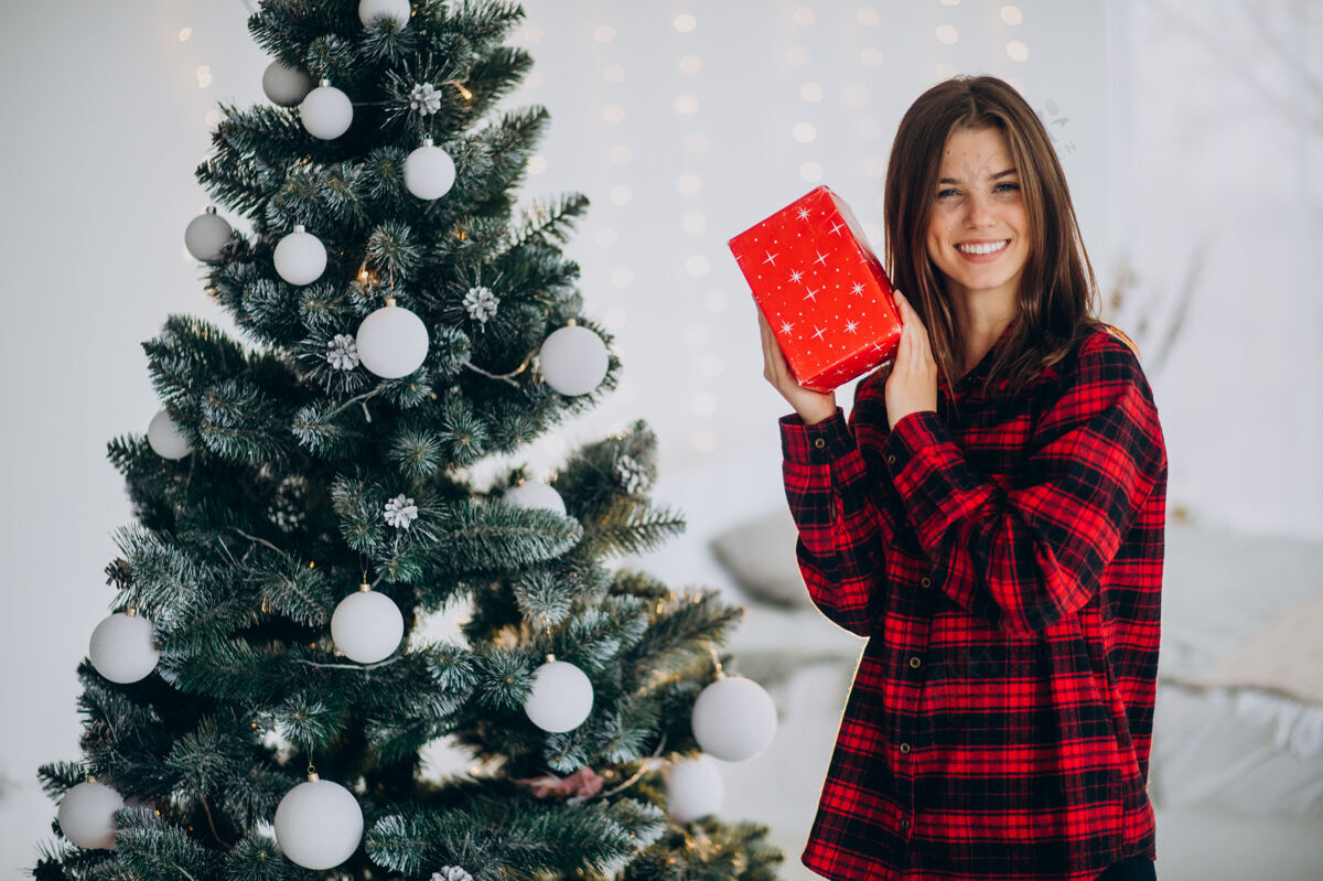 包装圣诞树边拿着礼品盒的年轻女子奢华惊喜圣诞节