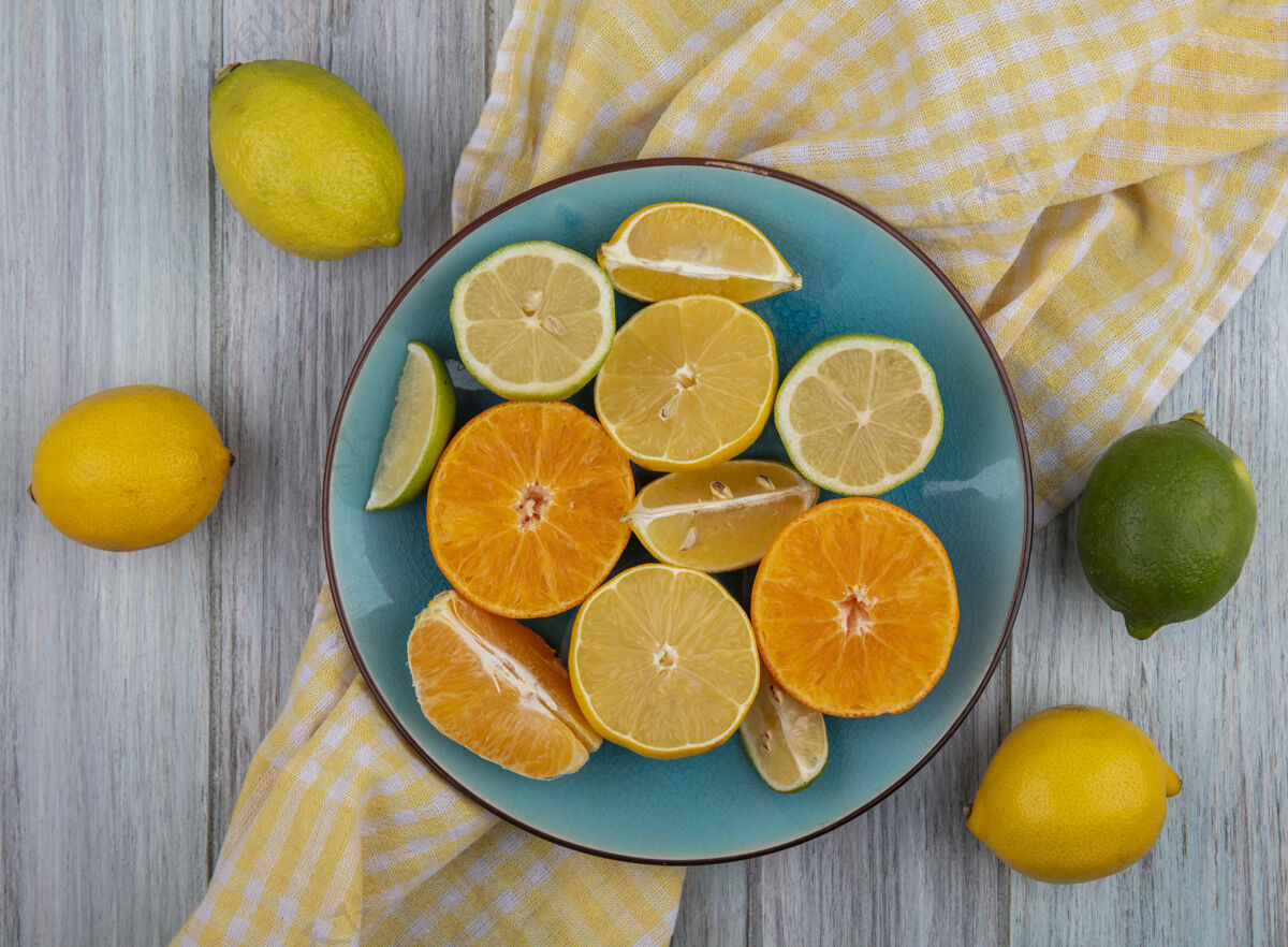 酸橙顶视图柠檬楔与石灰和橙色的盘子上的黄色格子毛巾在灰色的背景视野楔形柠檬色